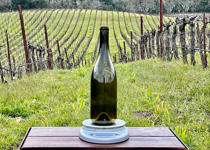 Logo bottle on scale with vineyard in background Logo bottle on scale with vineyard in background